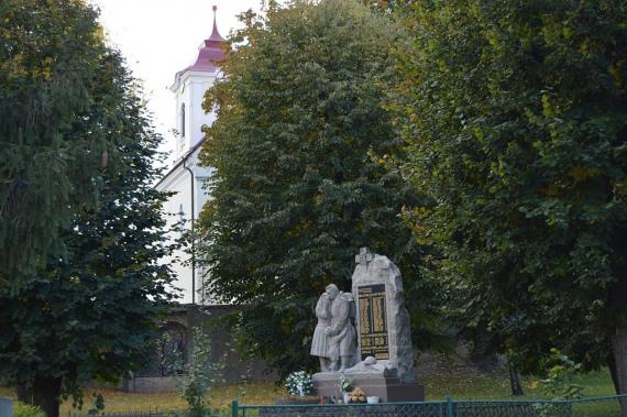 Pohľad na pomník v pozadí v múre Lurdská kaplnka a farský kostol Pohľad na pomník v pozadí v múre Lurdská kaplnka a farský kostol